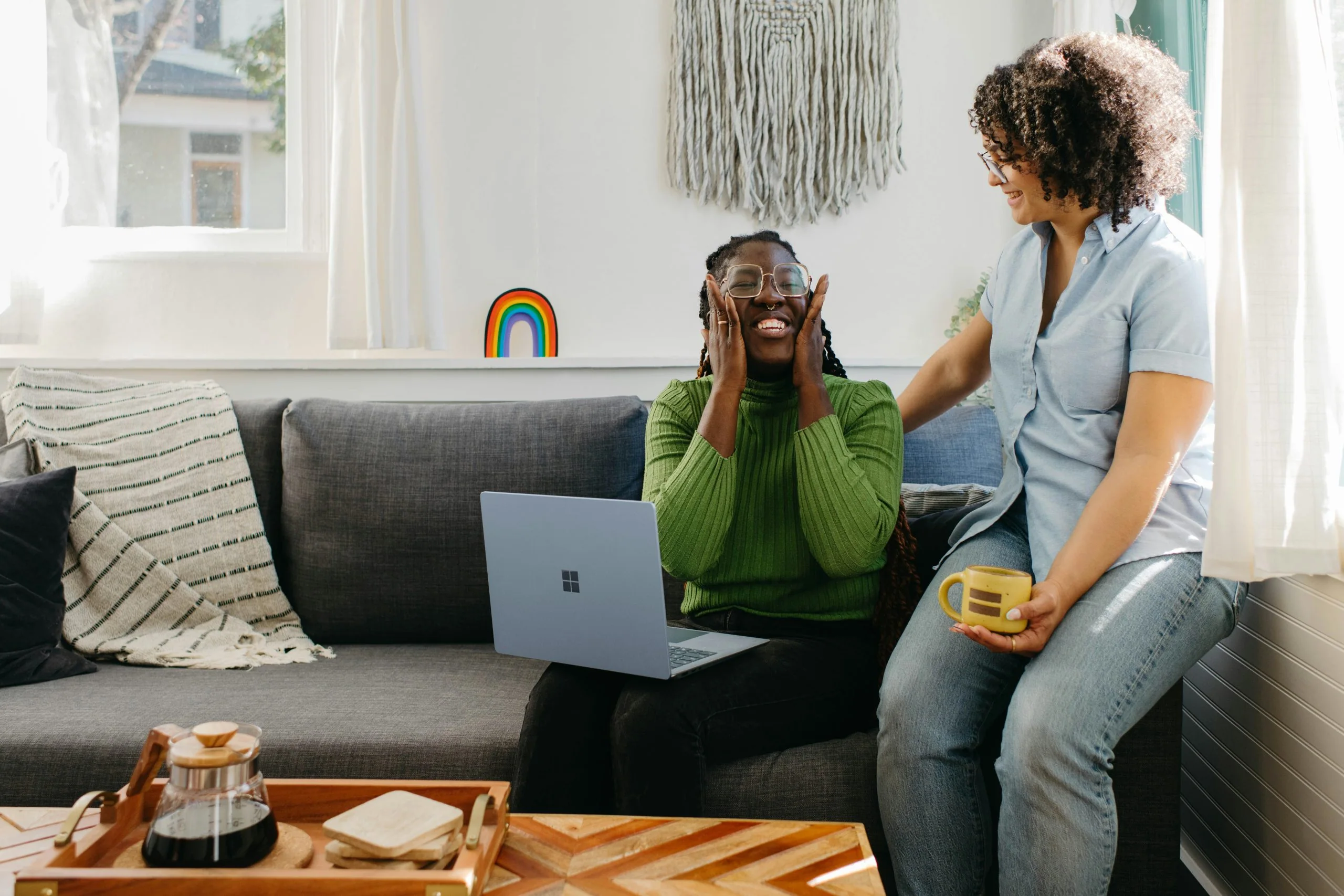 two diverse women talking and laughing while working on a gray couch